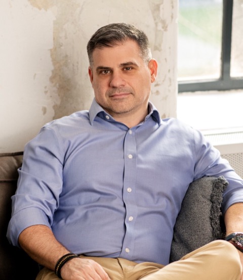 Gáspár András világos kék ingben, kanapén ülve, a kamerába nézve